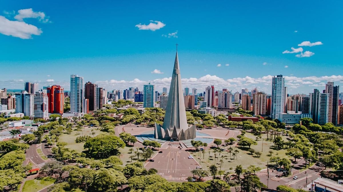 Vista aérea de Maringá com a Catedral Basílica ao centro, cercada pelas árvores da Praça da Catedral e pelos prédios do centro