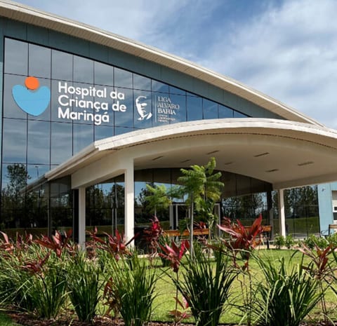 Fachada curva e envidraçada do Hospital da Criança de Maringá, com jardim na frente