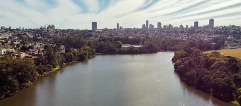 Vista do Lago Jaboti, em Apucarana, com a mata nas margens e o skyline da cidade no alto ao fundo