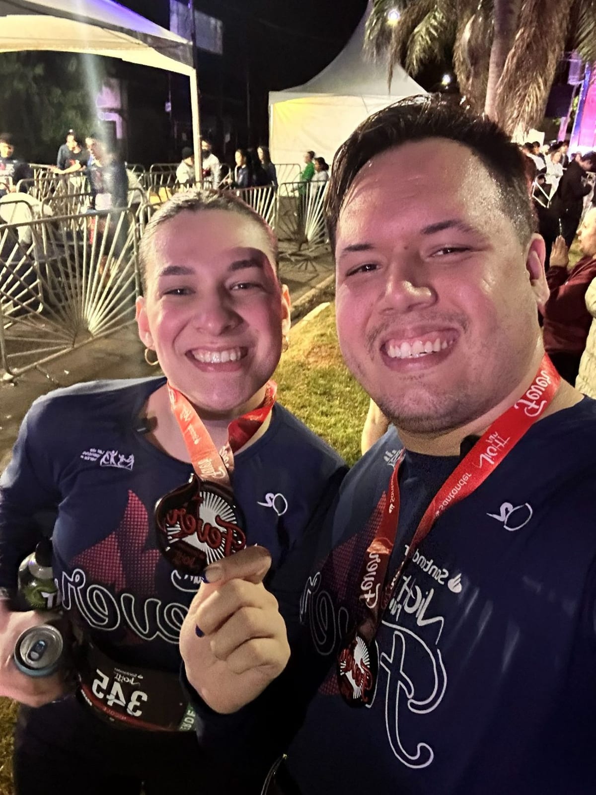 Casal sorrindo com medalhas ao final de uma corrida de rua noturna em Maringá
